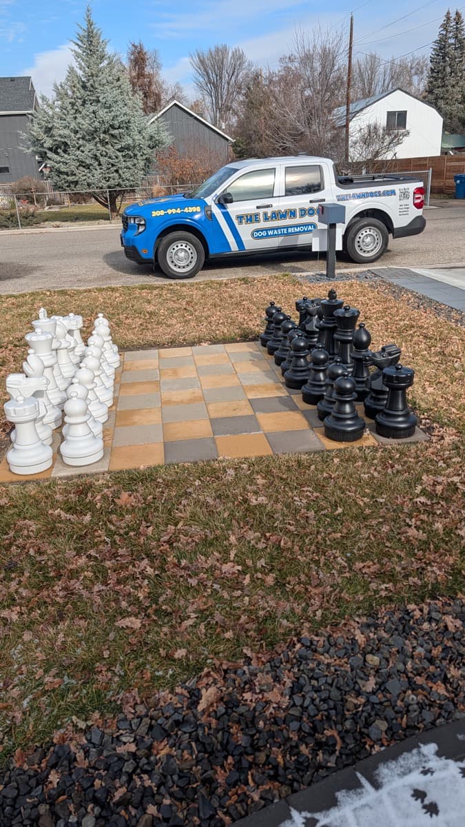 A Lawn Dogs truck parked at the curb outside a client's home, with a giant outdoor chess set laid out on the front lawn