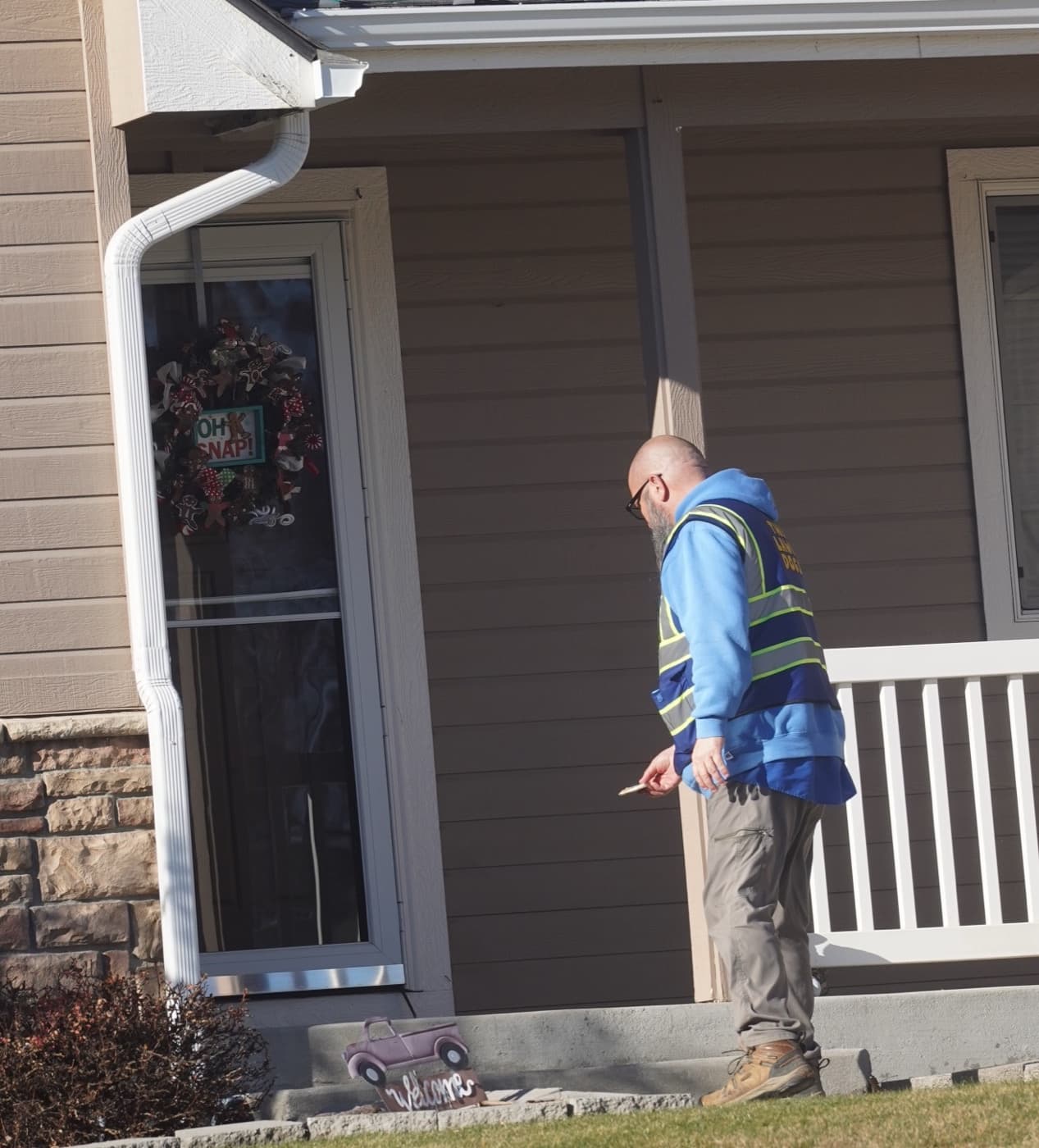 A Lawn Dogs technician in a branded vest leaving a dog treat at a client's front door