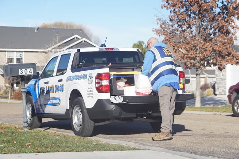 A Lawn Dogs technician loading bagged waste into the bed of a wrapped company truck at the curb
