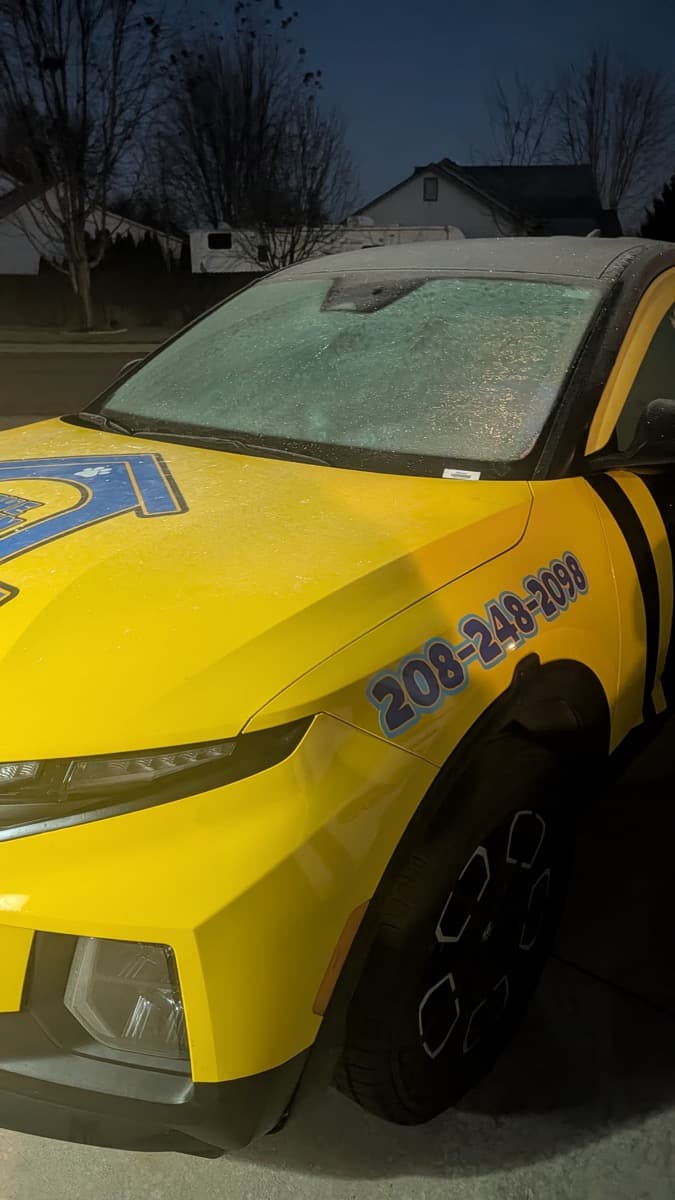 A Lawn Dogs truck with a frost-covered windscreen parked in a driveway before dawn, about to start a winter route