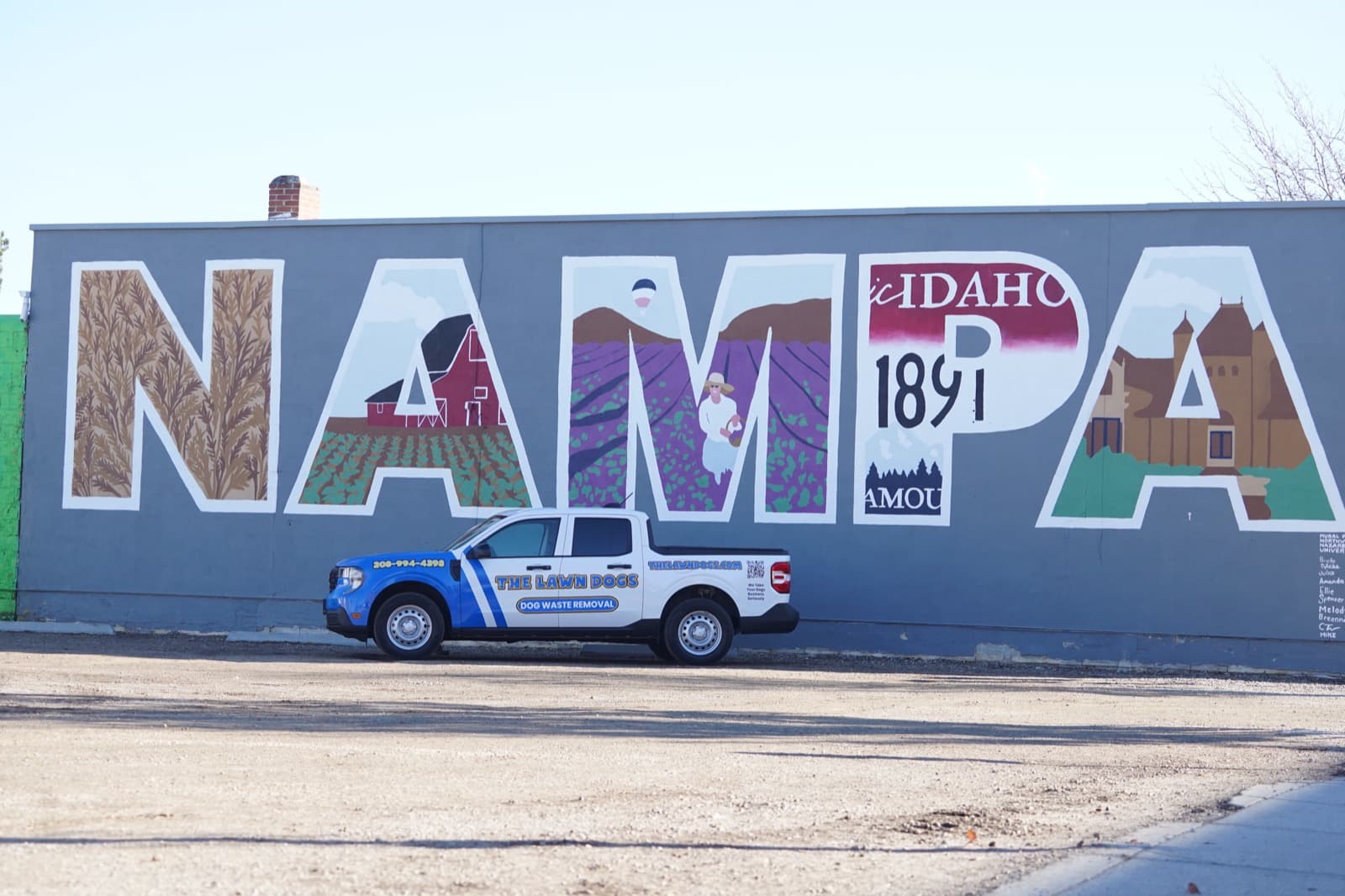 A wrapped Lawn Dogs truck parked in front of the large NAMPA mural in downtown Nampa, Idaho