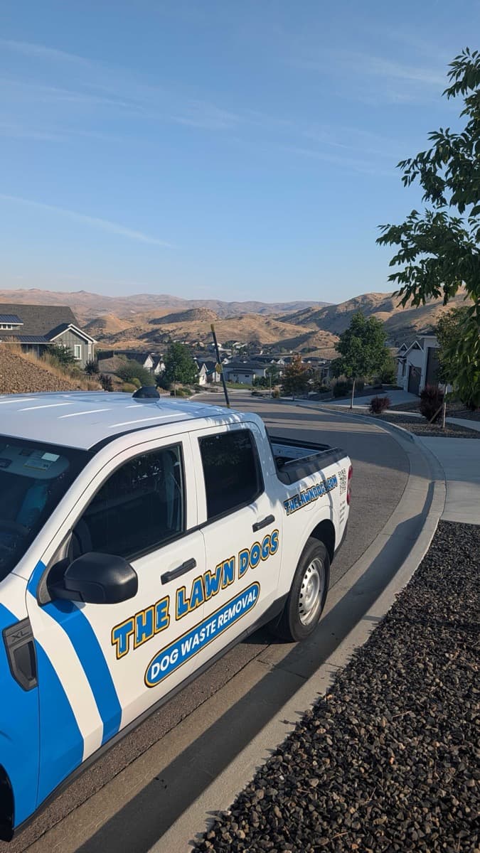 A Lawn Dogs truck on a curving foothill road above the Avimor community, with the valley and homes below