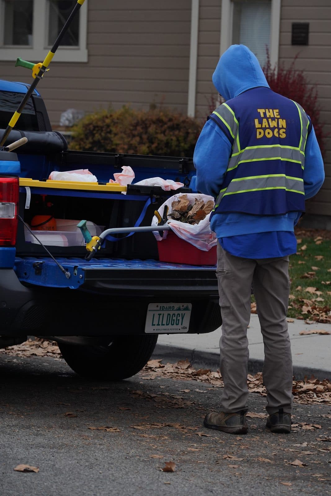 Lawn Dogs technician at the back of an open truck bed with a rake, bin and bagged yard debris